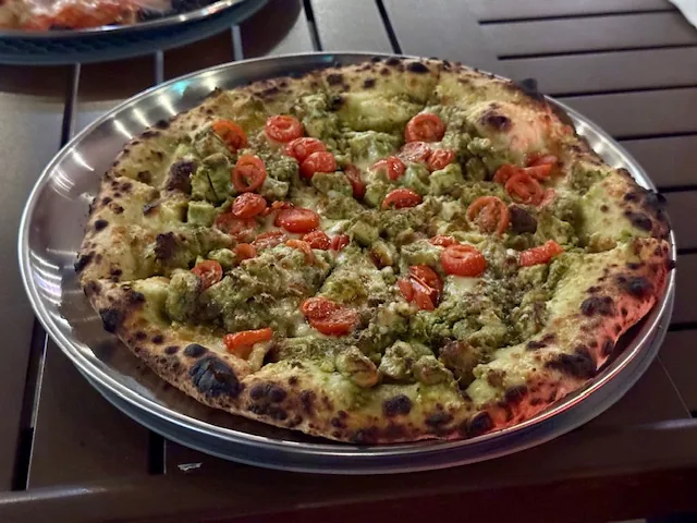 Freshly baked pesto chicken pizza with cherry tomatoes served at a catered event