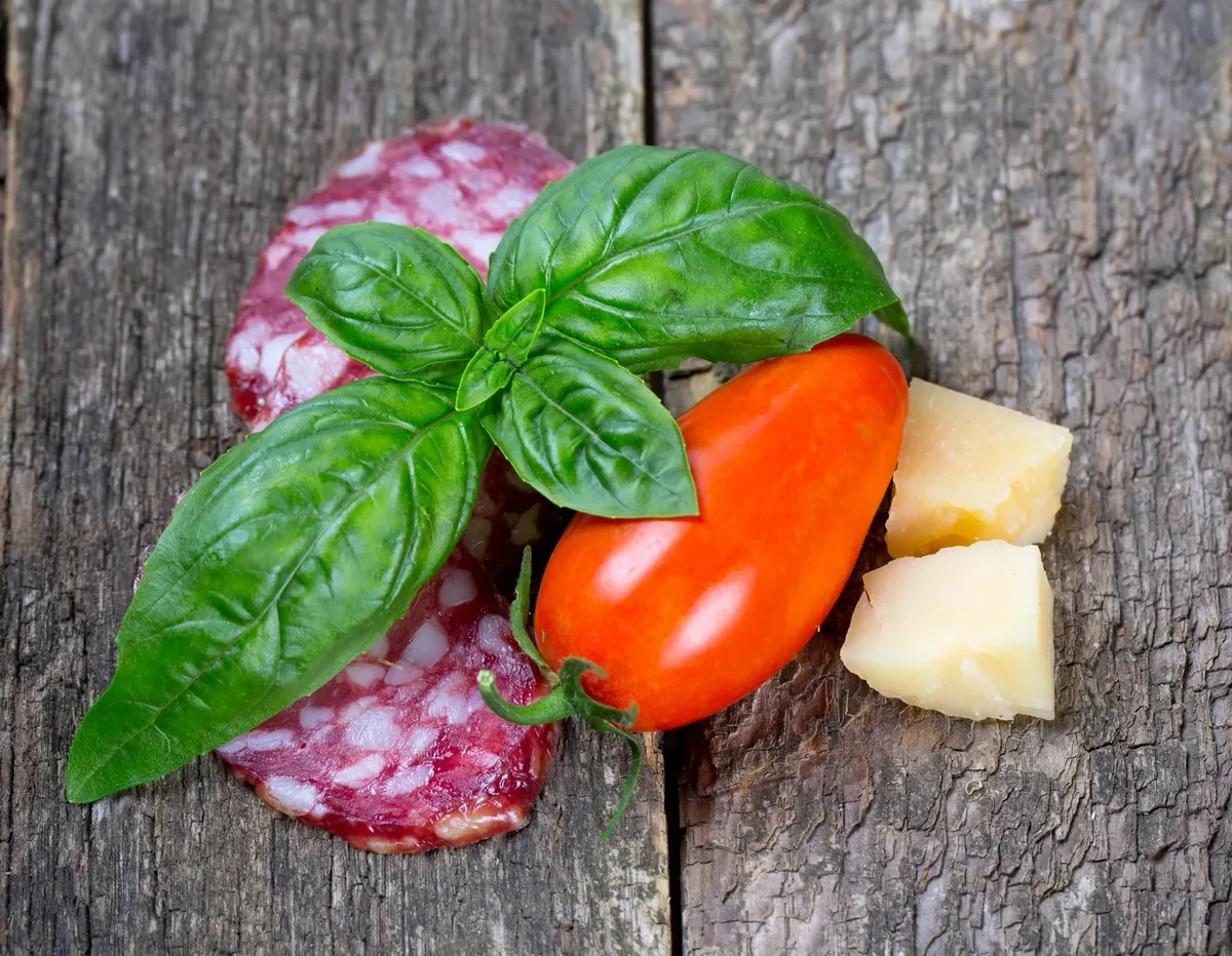 Fresh basil, salame, a San Marzano tomato, and Parmigiano-Reggiano on a rustic wood table
