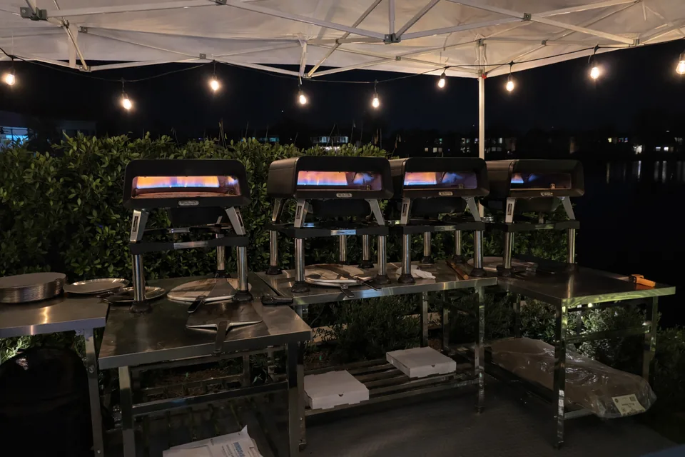 Four ovens glowing under string lights at an evening event