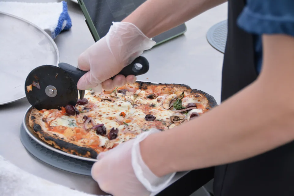 Slicing a fresh pizza with a roller cutter during service